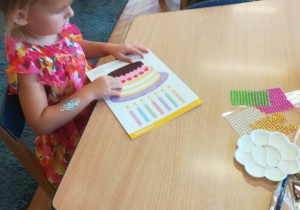 Dziewczynka ozdabia koralikami tort wydrukowany na kartce